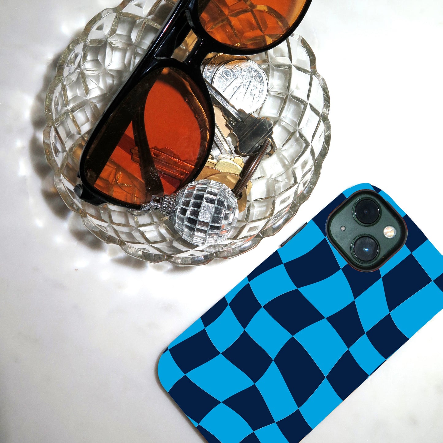 Sunglasses on a glass dish with a blue and black checkered phone case next to it.